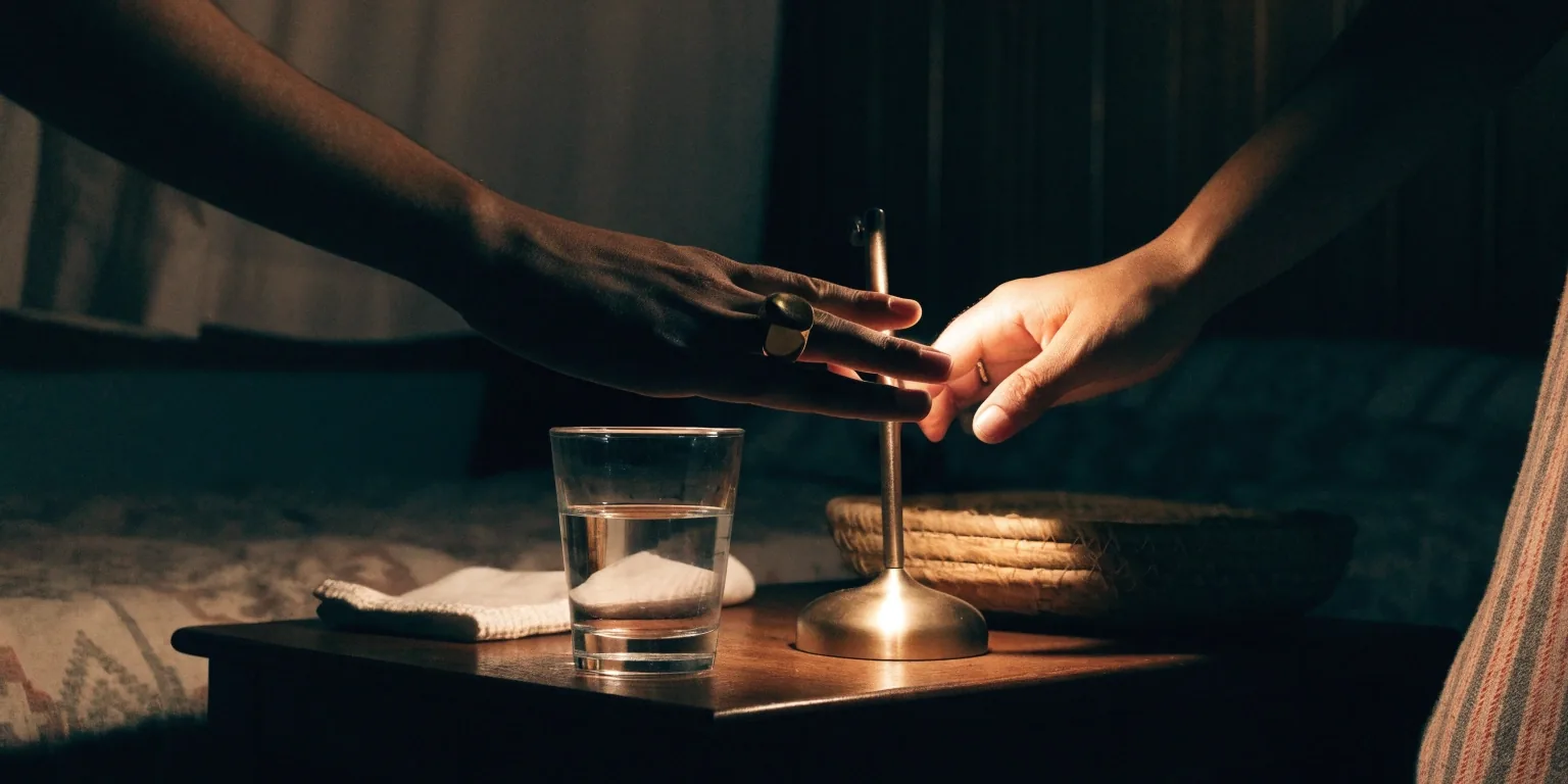 A quiet bedside table at night in a Botswana bedroom with a glass of water and a dimmed lamp